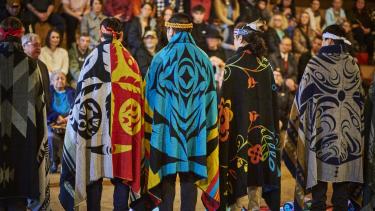 Five Indigenous Role Models blanketed and stand in the longhouse in front of their peers