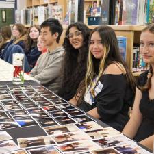 Students sitting at table, ready to hand out photos and certificates