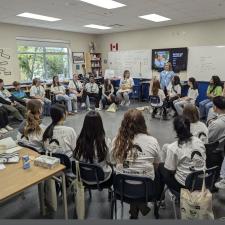 Students seated and gathered in chairs in a circle around a classroom.