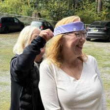 Two women, with one tying a bandana around the head of the other.